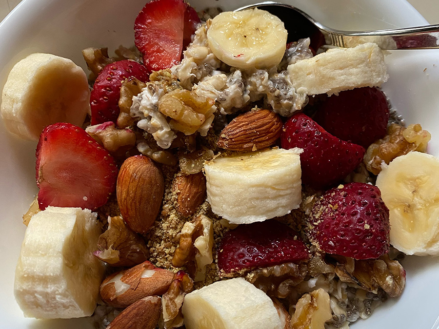 A healthy breakfast bowl filled with oatmeal and chia seeds, topped with sliced bananas, fresh strawberries, whole almonds, and walnuts.